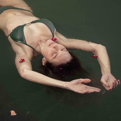 Frau in einem dunkelgrünen Bikini treibt entspannt im Wasser, umgeben von roten Blüten